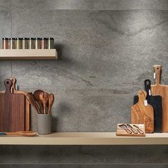 kitchen utensils and wooden cutting boards on a shelf in front of a gray wall