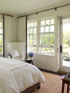 a white bed sitting in a bedroom next to two large windows on either side of the bed