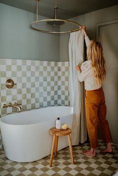 a woman is standing in front of a bathtub and holding the shower curtain open