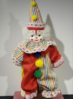 a clown statue with a red and white striped suit on it's head, holding a yellow pom - pom