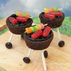 three chocolate desserts with marshmallows and candy on sticks sitting on a wooden board