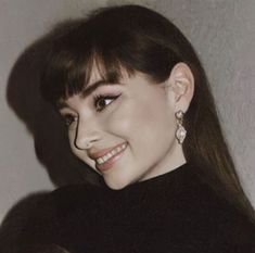 a close up of a person with long hair wearing earrings and smiling at the camera