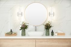 a bathroom vanity with a round mirror above it and flowers in vases on the counter