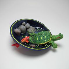 a ceramic turtle sitting on top of a bowl filled with rocks