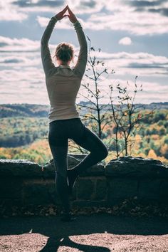 a woman is doing yoga on top of a hill with her hands in the air