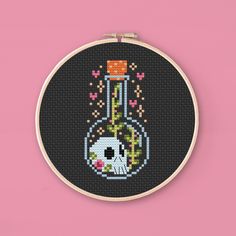 a cross stitch pattern with a vase filled with flowers on a pink background, in the shape of an embroidery hoop