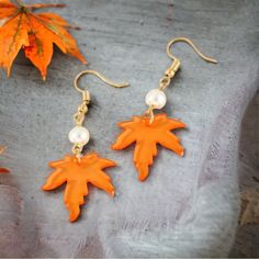 two pairs of earrings with orange leaves and pearls hanging from the ear hooks on a gray surface