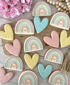 decorated cookies with pastel rainbows and hearts on a wooden board next to pink flowers