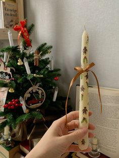 a person is holding a lit candle in front of a christmas tree and an open book