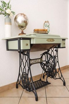 an antique sewing machine table with flowers and books on the top, next to a globe