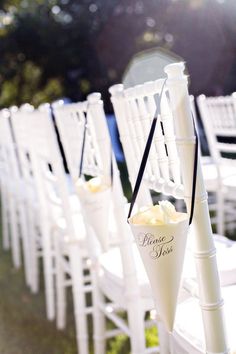 rows of white chairs with black ribbons and flower arrangements on them for an outdoor wedding ceremony