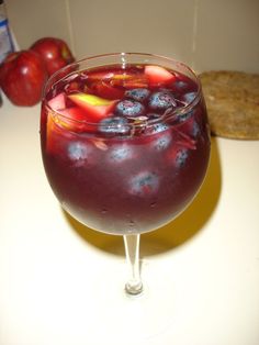 a glass filled with liquid and fruit on top of a white counter next to an apple