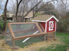 a chicken coop with a red barn in the back ground and grass on the other side