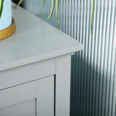 a plant is sitting on top of a white dresser next to a wall with vertical blinds