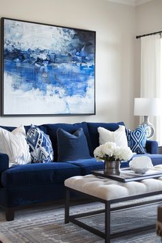 a living room with blue couches and white pillows on the table in front of a large painting