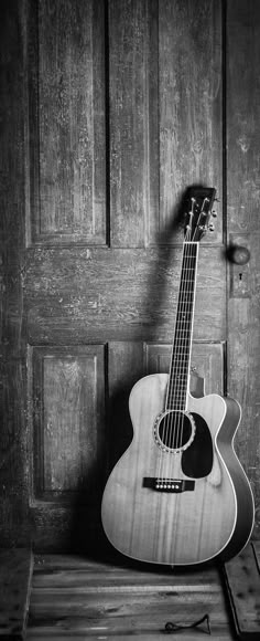 an acoustic guitar sitting on top of a wooden box in front of a wood door