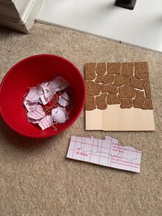 a red bowl filled with pieces of paper next to a cut out piece of wood