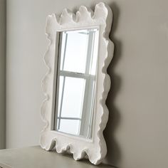 a white decorative mirror sitting on top of a dresser next to a window in a room