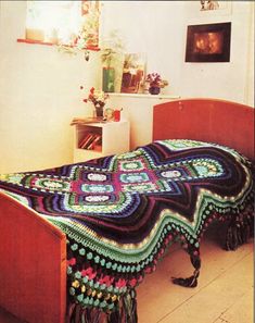 a crocheted blanket on a bed in a room with white walls and wooden floors