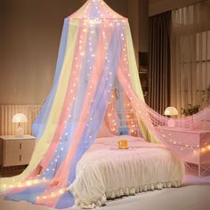 a bed with a pink and blue canopy over it's headboard covered in fairy lights