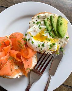 a white plate topped with an open face sandwich and sliced up avocado next to a fork