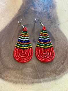 These handmade beaded earrings are truly unique. Each one is hand made with a rotating striped pattern. These earrings are available in a multitude of colors -making them perfect for any outfit! Whether it's dressing up a jean jacket or adding a unique texture to a LBD, there's no way you can go wrong with these earrings! We have given each design a name in honor of our favorite people! Please note that colors may vary a bit by pair as no two are exactly alike Multicolor Fair Trade Beaded Earrings For Festival, Fair Trade Multicolor Beaded Earrings For Festival, Multicolor Fair Trade Beaded Earrings, Casual Multicolor Fair Trade Jewelry, Adjustable Multicolor Earrings With Large Beads, Bohemian Multicolor Wooden Bead Earrings, Handmade Casual Beaded Earrings, Casual Multicolor Teardrop Earrings, Casual Handmade Beaded Earrings