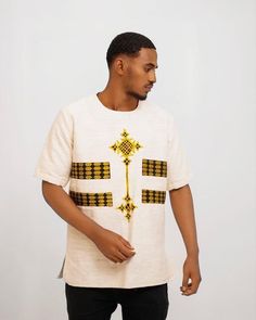 This traditional Ethiopian shirt for men is handmade from high-quality fetil fabric, which is known for its softness and durability. The shirt features a unique tilf detailing, which is a decorative panel that runs along the bottom of the shirt. The tilf is adorned with intricate embroidery and patterns, adding to the beauty and elegance of the shirt. The fetil fabric is breathable and lightweight, making it perfect for warm weather. The shirt is designed with a collarless neckline and a loose, Traditional Crew Neck Cotton Shirt, Traditional Cotton Crew Neck Shirt, Traditional Fit Cotton Tops For Summer, Traditional Fit Cotton Summer Tops, Traditional White Shirt For Festivals, Traditional White Cotton T-shirt, Traditional Embroidered Cotton T-shirt, Traditional Fit White Top, White Traditional Tops With Traditional Patterns