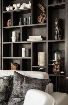 a white couch sitting in front of a book shelf filled with vases