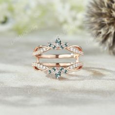 a rose gold ring with green and white diamonds in the middle, on top of sand