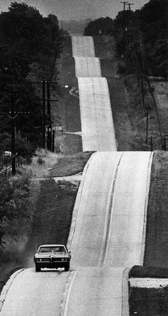 a black and white photo of a car driving down a road next to a waterfall