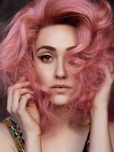 a woman with pink hair is posing for the camera and has her hands on her head