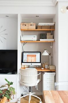 a desk with a computer on top of it in front of a wall mounted television