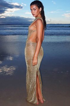 a woman standing on top of a sandy beach next to the ocean wearing a gold dress