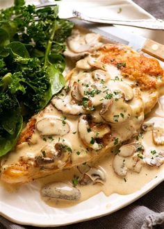 a white plate topped with meat covered in mushroom sauce and greens next to a fork