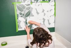 a woman is painting the wall in her bathroom with green paint and white flowers on it