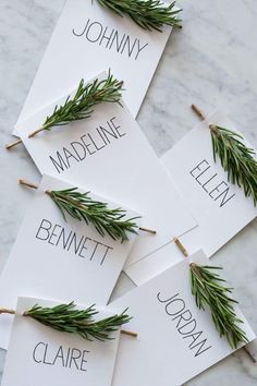 four place cards with rosemary on them are sitting on a marble countertop and have the names of each individual