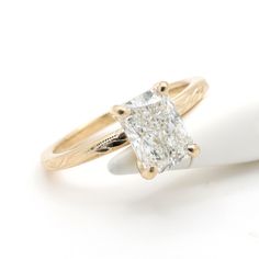 a yellow gold engagement ring with a princess cut diamond in the center on a white background