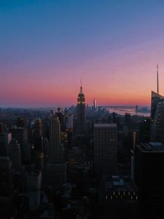 the city skyline is lit up at dusk with skyscrapers in the foreground and an ocean in the background