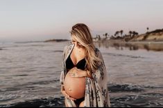 a pregnant woman standing on the beach with her belly wrapped up in a shawl