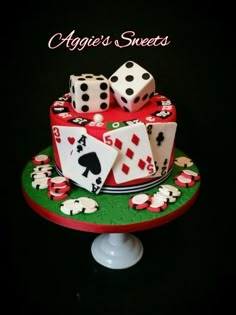 a cake decorated with playing cards and dices on top of a green plate that says aggie's sweets