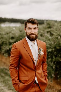 a man with a beard wearing an orange suit and flower in his lapel is posing for the camera