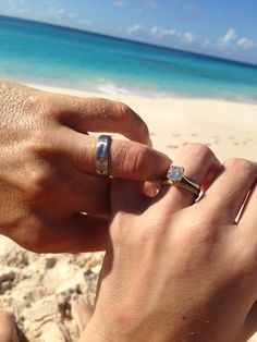 two people holding hands on the beach with their wedding rings in each other's hand