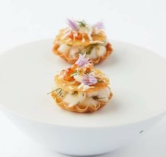 three small appetizers on a white plate with flowers in the middle and garnishes