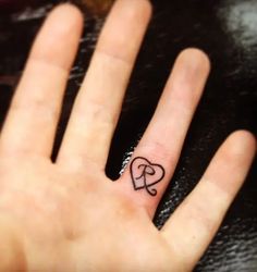 a person's hand with a small heart tattoo on the middle finger and an arrow in the middle