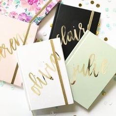 three notebooks with gold foil lettering on them and confetti around the edges