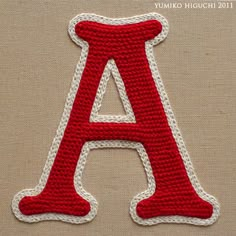 a crocheted letter is shown in red, white and grey yarn with the letter a on it