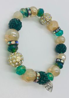 "The highlight of this handmade beaded stretch bracelet is the emerald and gold sparkle ball beads. These colourful crystallized beads complement the iridescent crystal spacer beads in antique gold throughout the bracelet. The rest of the bracelet is made up of green and gold beads in a variety of shapes, sizes and iridescent sheens. As the bracelet moves with wear the beads catch the light, emphasizing the unique sparkle and shimmer of the piece.  Each piece of jewelry from my store features the signature \"made with love\" heart charm. Includes a white organza bag to store." Gold Crystal Bracelets With Colorful Beads, Green Crystal Bracelet With Colorful Beads, Green Stretch Bracelet With Faceted Round Beads, Green Beaded Bracelet With Gold Beads, Green Crystal Round Beads Bracelets, Green Crystal Beaded Bracelets With Round Beads, Green Crystal Beaded Bracelets, Sparkle Ball, Iridescent Crystal