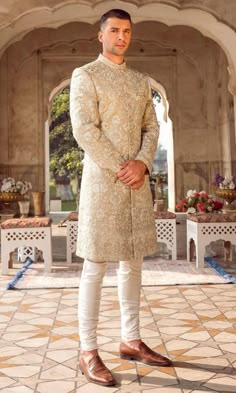 a man standing in front of an archway wearing a beige sherve and white pants