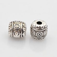 two silver plated beads, one with an ornate design and the other has a hole in