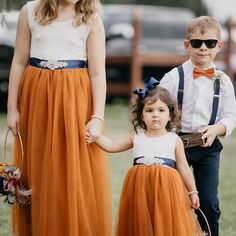 two young children wearing orange tulle skirts and bow ties, one holding the hand of an adult